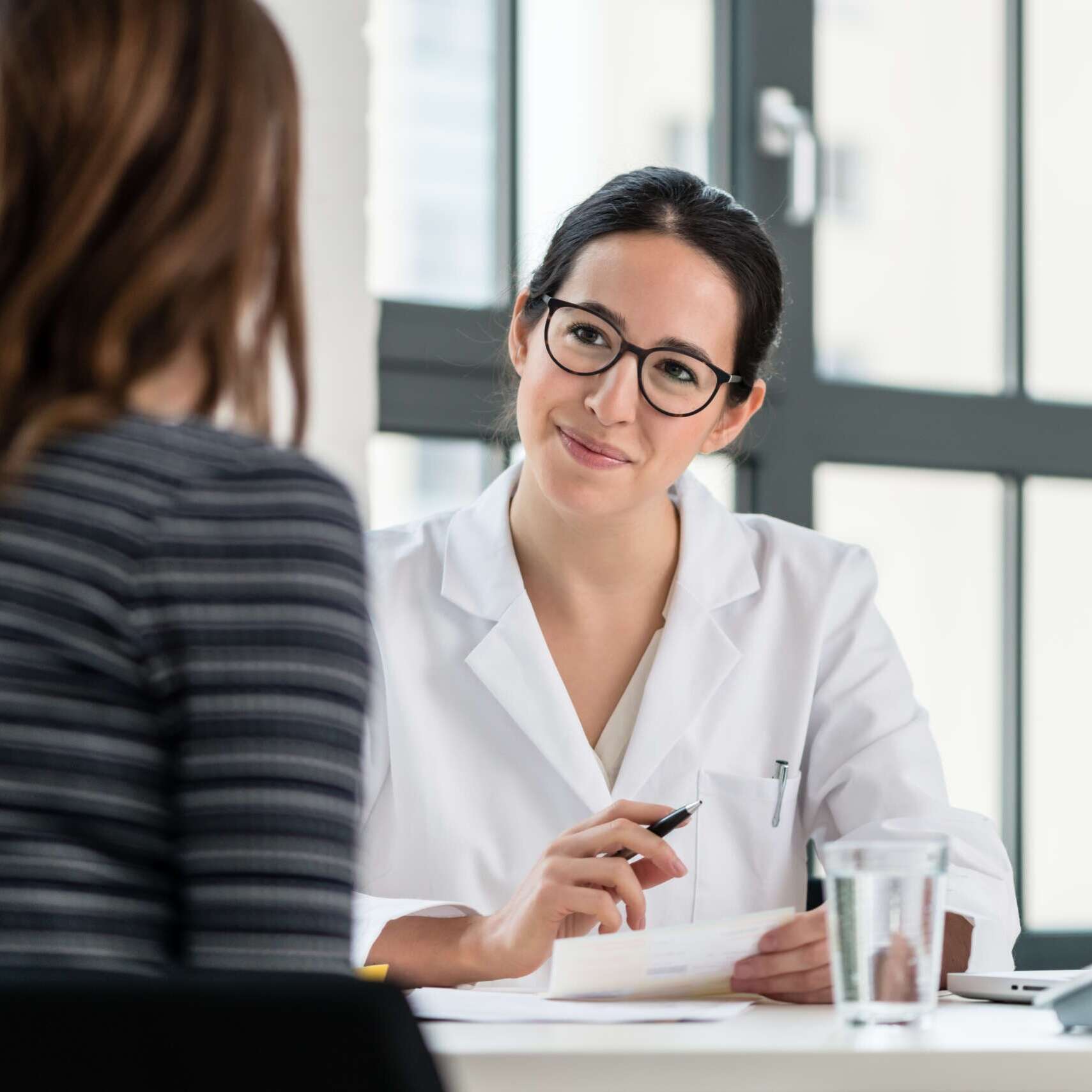 Female physician listening to her patient during consultation while sitting down in the office of a modern medical center